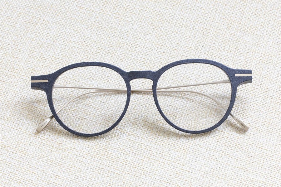 Monture ronde en bio-nylon bleu Y.Neuman, posée sur une toile de lin.