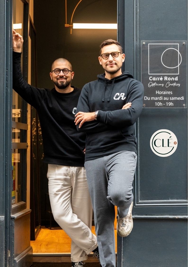 Christophe et Louis devant Carré Rond Opticiens à Lyon, le macaron CLÉ apposé en vitrine.